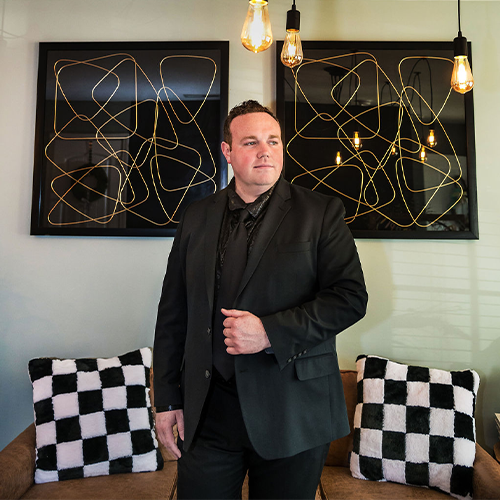 Caleb Butler in an all black suit in front of abstract art