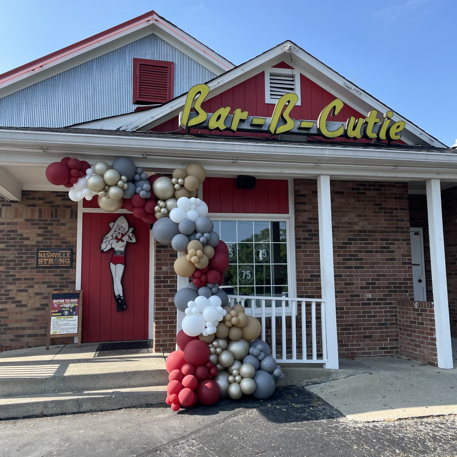 a beautiful red, white, gray, and tan balloon half arch over the bar-b cutie entrance