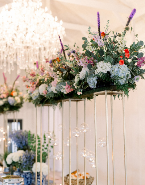 Buffet table with tall gold stands topped with lush pastel florals and hanging glass orbs under a crystal chandelier