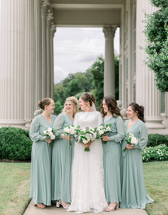 bridesmaids stand with the bride in front of pillars